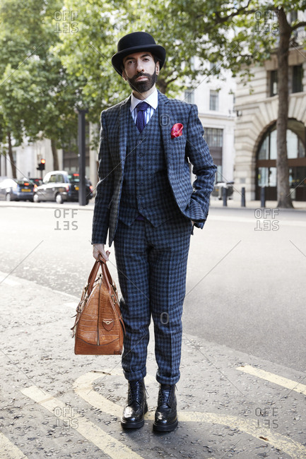 London, England - June 9, 2017: Bearded man wearing three piece blue checked suit and bowler hat holding a hold all in the street during London Fashion Week Men's
