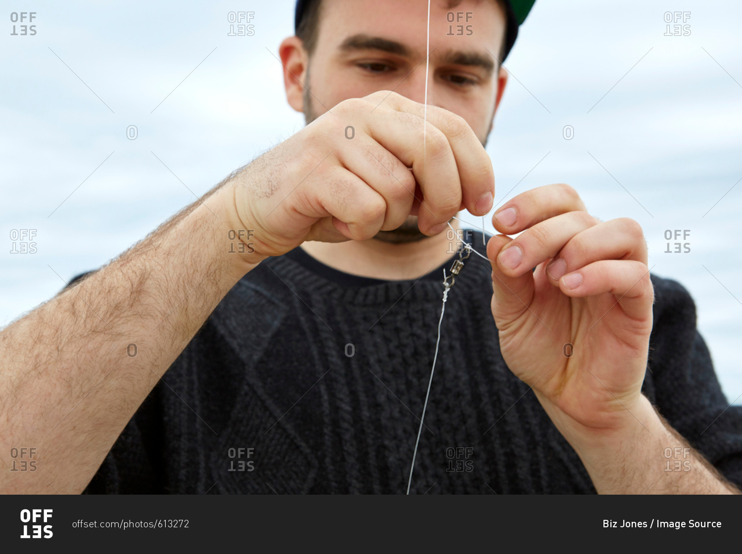Young man attaching fishing hook to fishing line