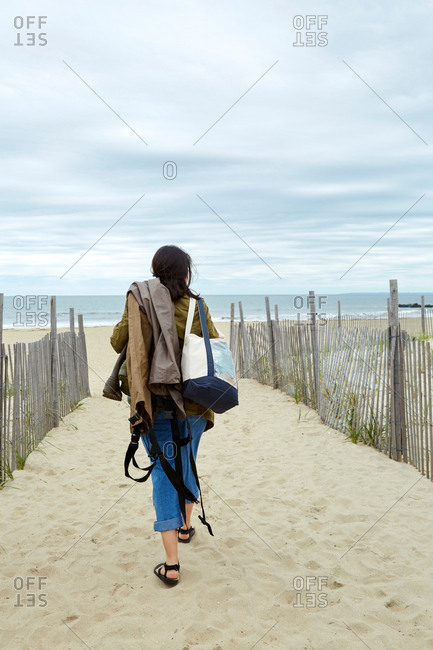 Rear view of young woman carrying sea fishing equipment on beach