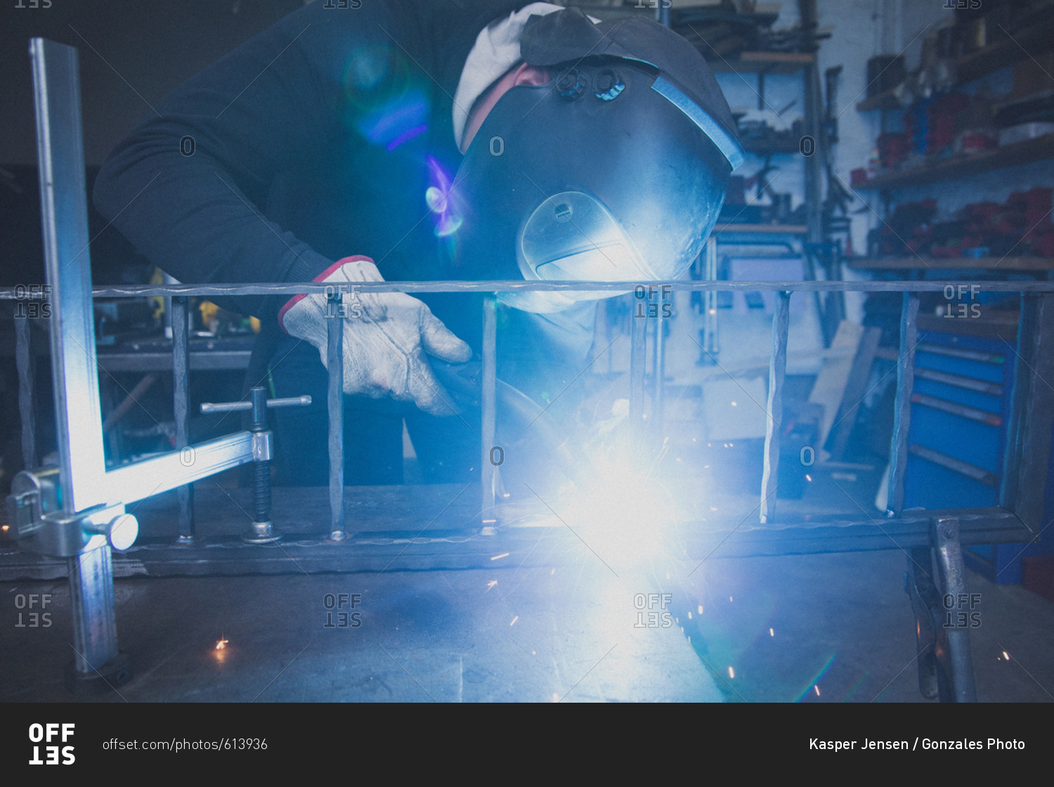 A blacksmith wears safety gear and is welding a metal construction in a metalsmith\'s workshop