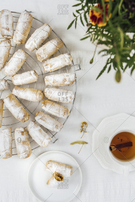 Turkish cookies stuffed with apple and cinnamon on a cooling rack on a white background photographed from top view. A cup of tea, a small plate with cookies and flowers accompany