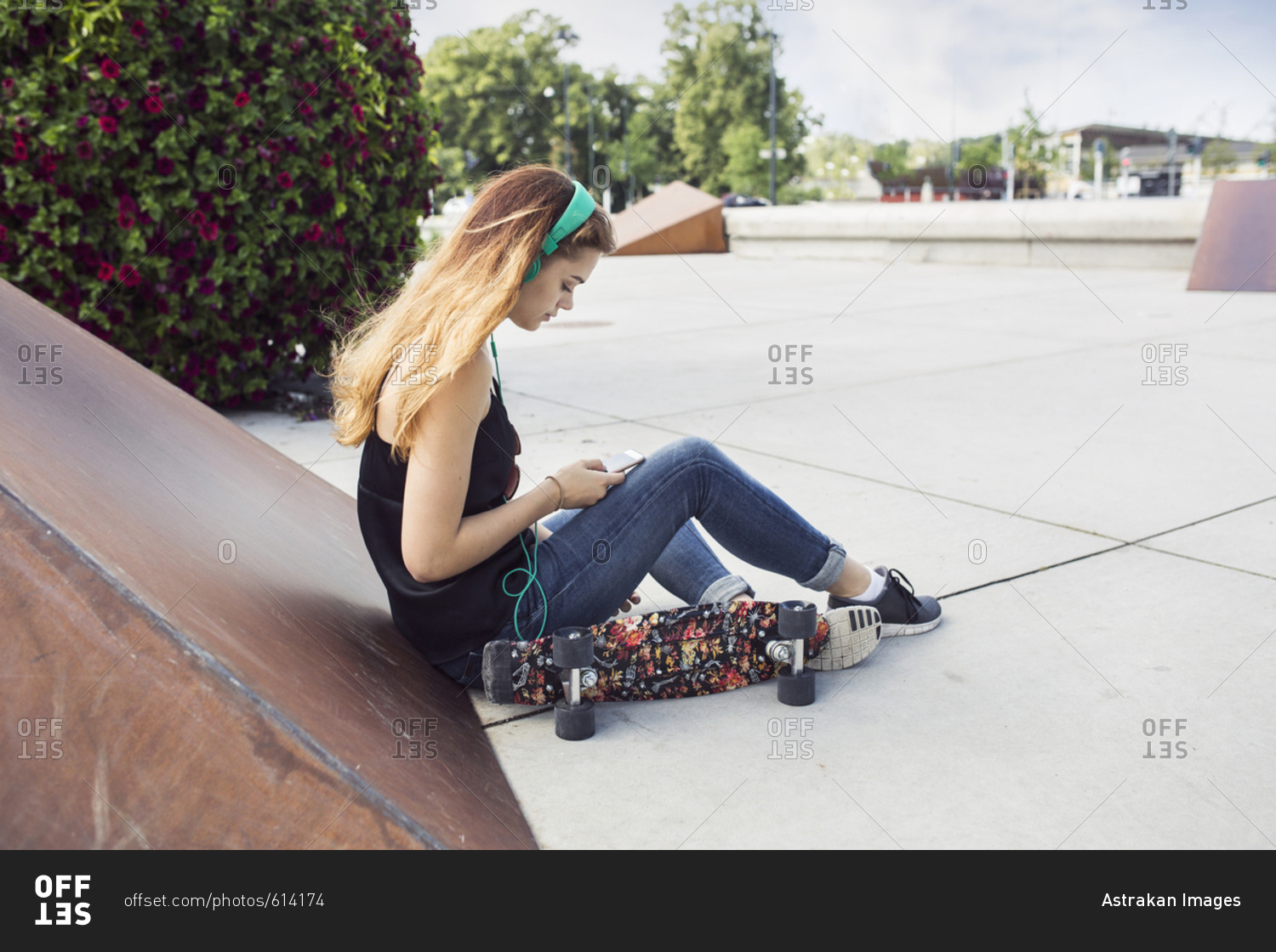 Teenage girl (14-15) sitting in skateboard park and listening to music