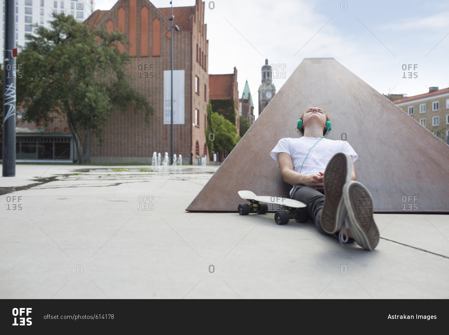 Teenage boy (16-17) sitting in skateboard park and listening to music