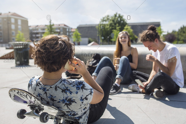 Teenage girls (14-15) and teenage boy (16-17) hanging out in skateboard park