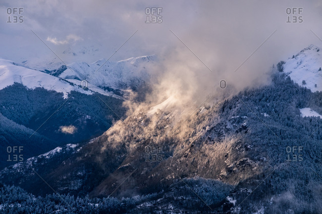 Horizontal outdoors shot of snowy winter mountain with forest covered with mist.