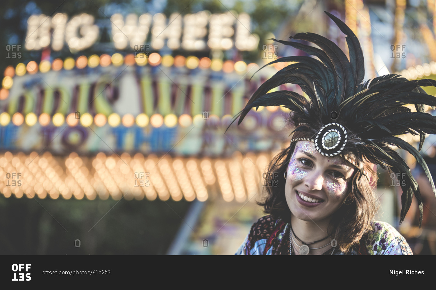 Girl wearing feather headdress in front of a carnival ride