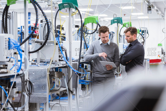 Manager and factory worker looking at digital tablet by factory machinery