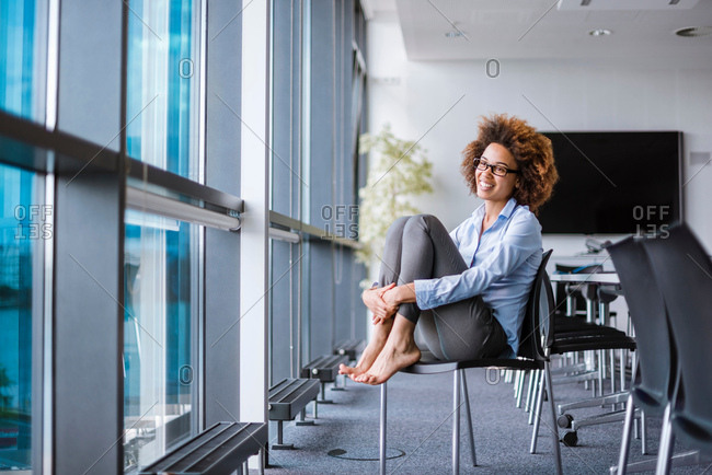 Happy barefoot young businesswoman sitting on office chair