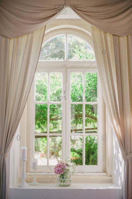 Curtains Around Curved Window With Vase Of Flowers And Candles On