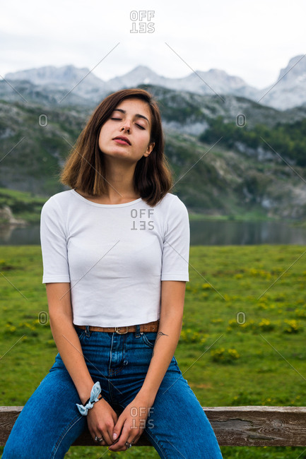Young woman with eyes closed resting in mountain meadow with eyes closed.