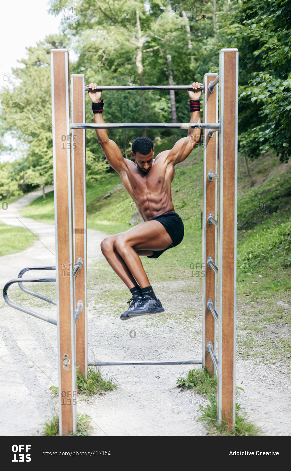 Shirtless muscular black man exercising and doing workout on bar in the park.