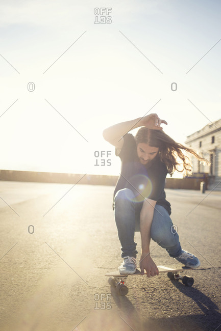 Young man long skateboarding on square in lights. stock photo - OFFSET