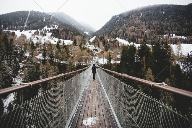 View of suspension bridge and female walking on it on snow-capped mountains background.
