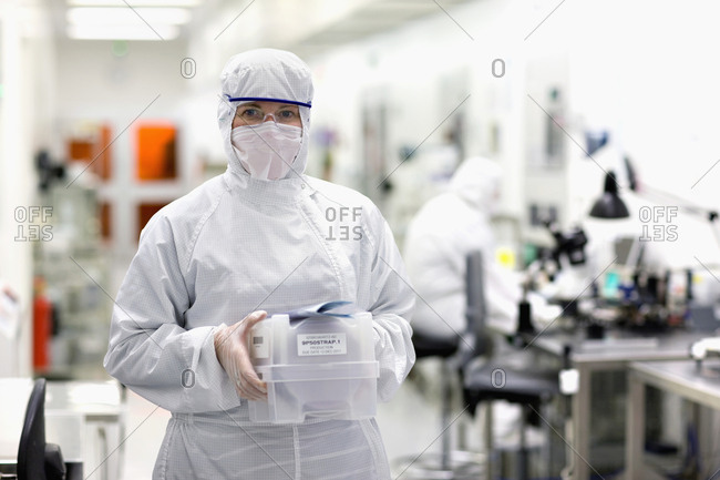 Portrait of scientist in clean suit carrying container in silicon wafer manufacturing laboratory