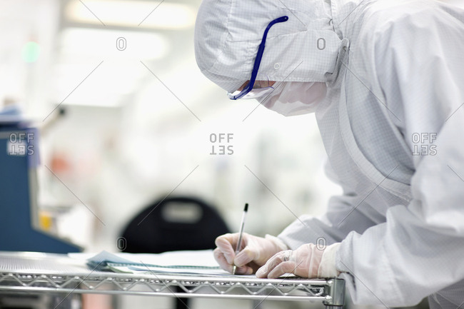 Engineer in clean suit taking notes in silicon wafer manufacturing laboratory