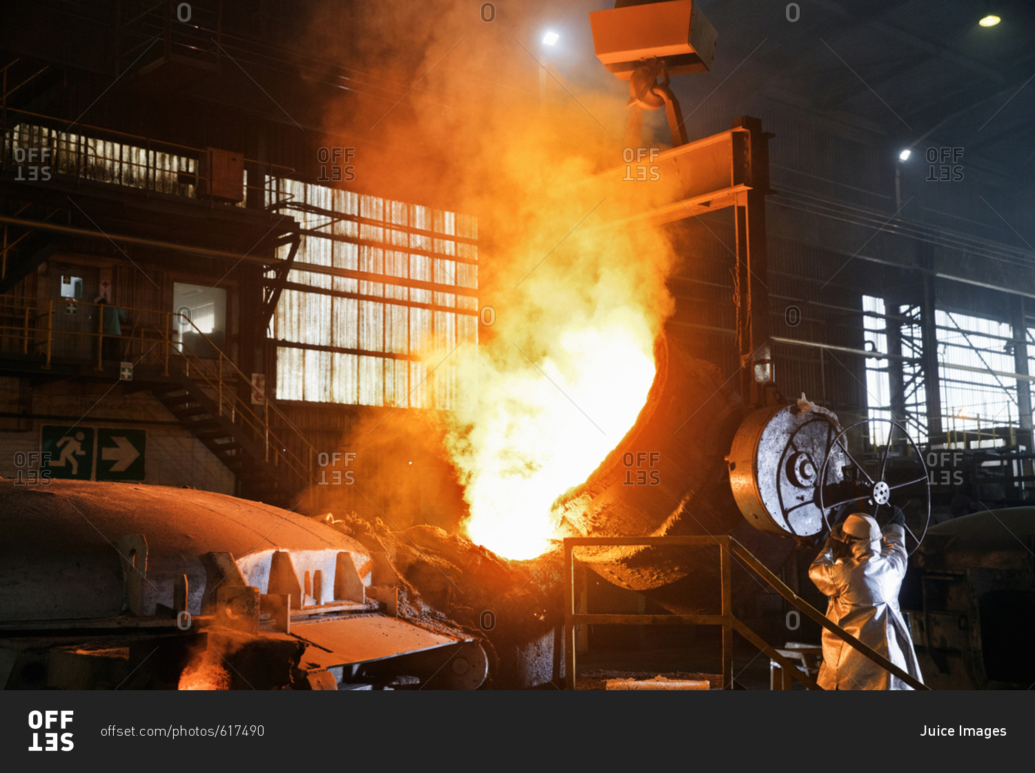 Worker In Protective Clothing Pouring Molten Metal In Foundry
