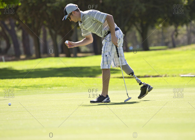 Male Golfer With Artificial Leg On Course Putting Ball On Green
