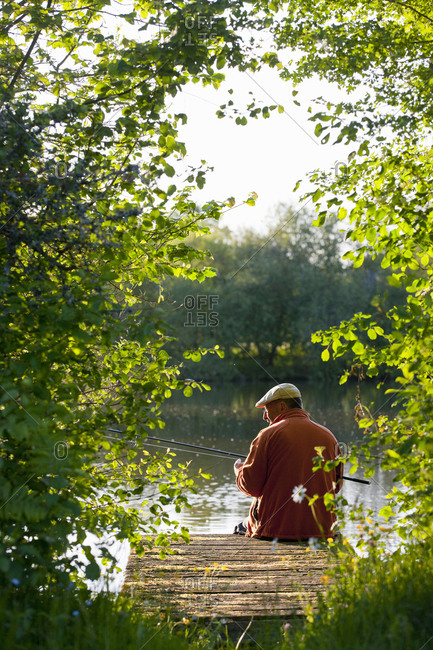 Fisherman fishing with rod on idyllic lake dock
