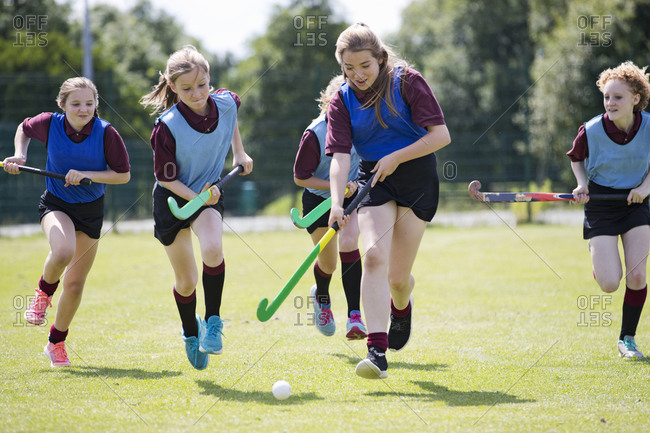 Middle schoolgirls playing field hockey on field in physical education class
