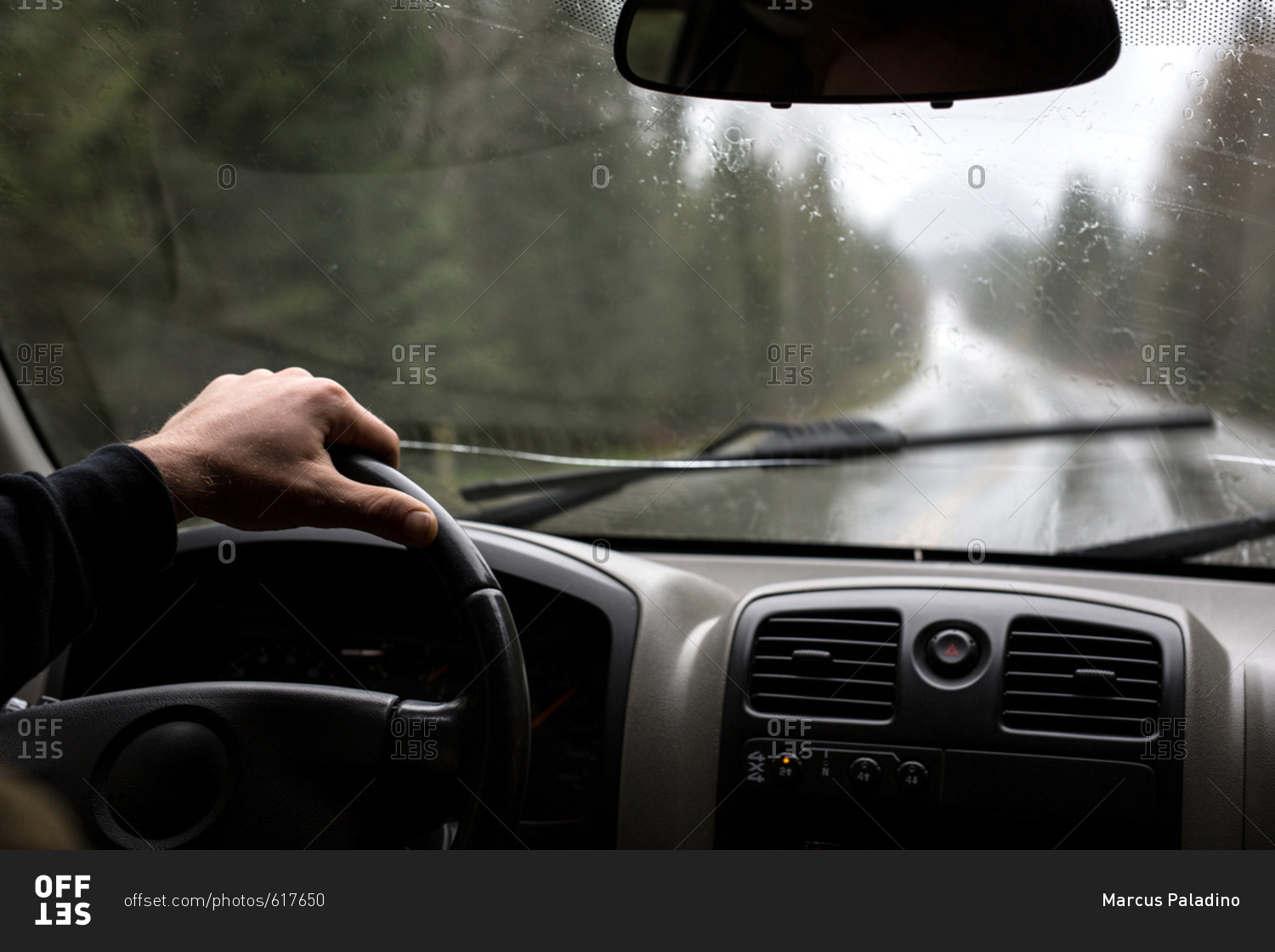Hand holding steering wheel while driving in the rain stock photo OFFSET