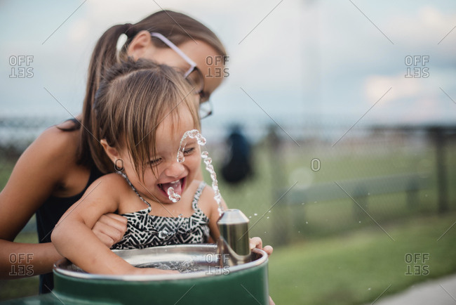 Girl helping sister at water fountain