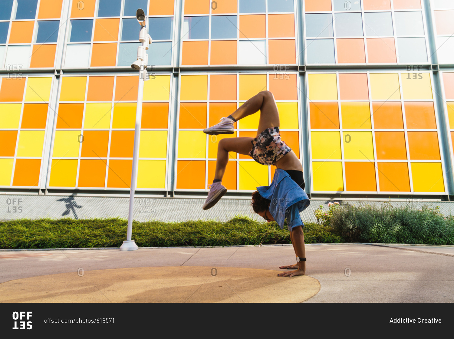 Side view of athletic girl posing in handstand on background of colorful building at street
