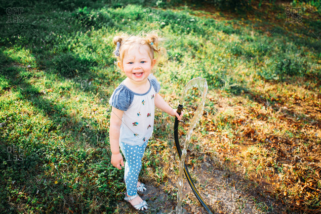 Smiling toddler girl playing with a garden hose