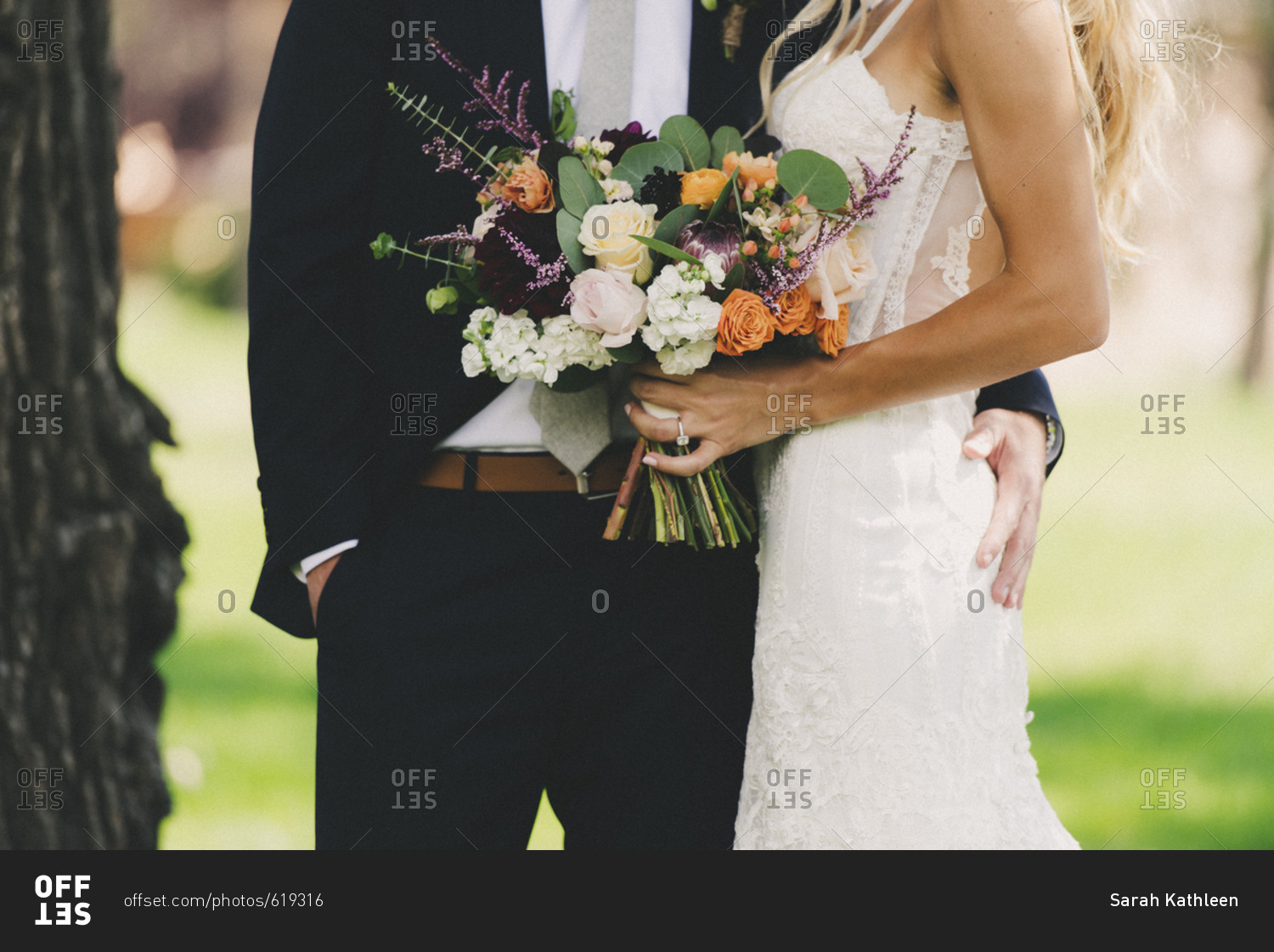 Mid-section portrait of bride and groom standing together with colorful bouquet