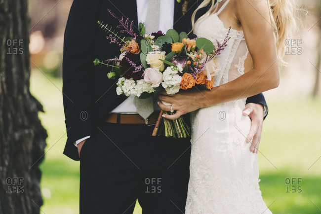 Mid-section portrait of bride and groom standing together with colorful bouquet