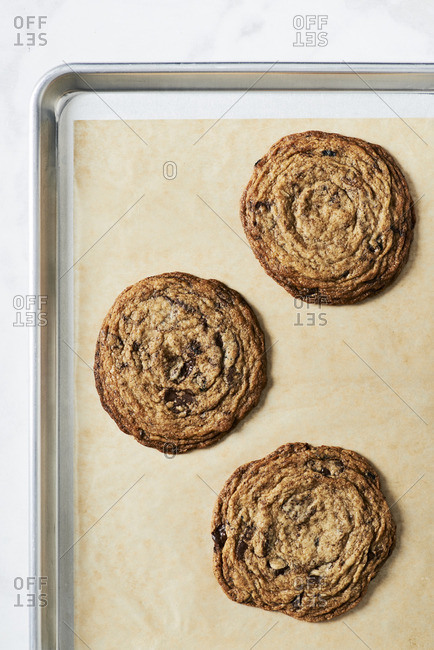 Four large chocolate chip cookies on a baking tray