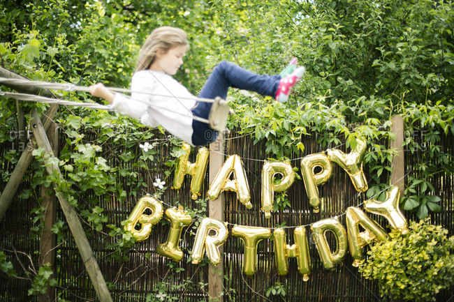 Decoration for Birthday Party in garden with golden balloons and swinging girl in the foreground