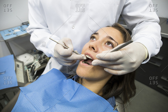 Unrecognizable dentist in latex gloves inspecting oral cavity of pretty patient.