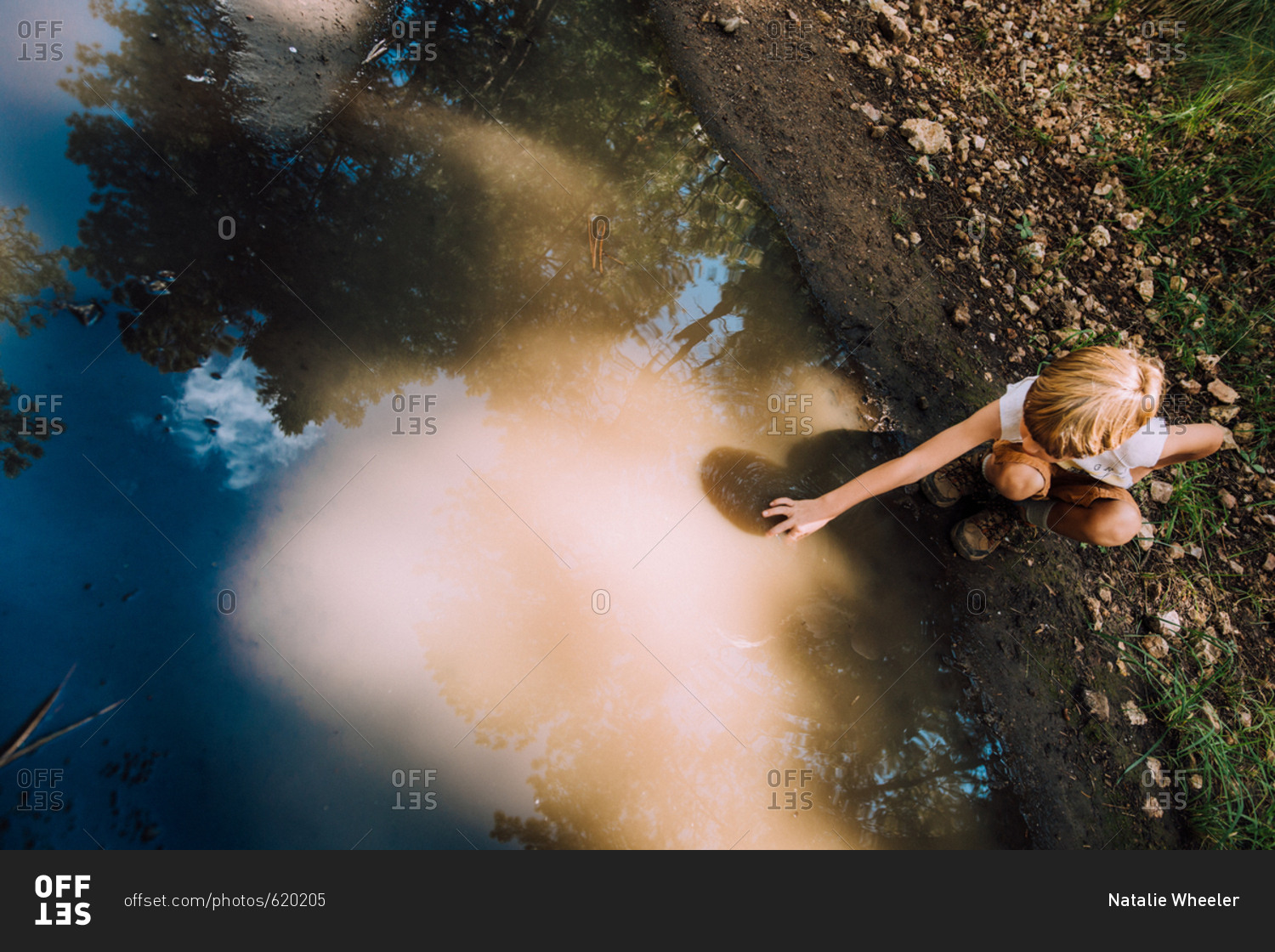 Boy reaching into mud puddle on dirt path