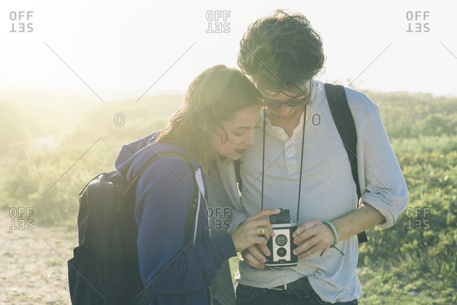 Young man with woman looking at retro camera while hiking on field during sunny day