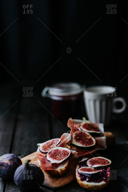 Bread with ham and fresh figs served on a wooden plate on dark background