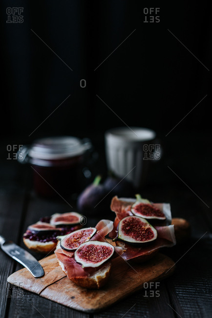Bread with ham and fresh figs served on a wooden plate on dark background