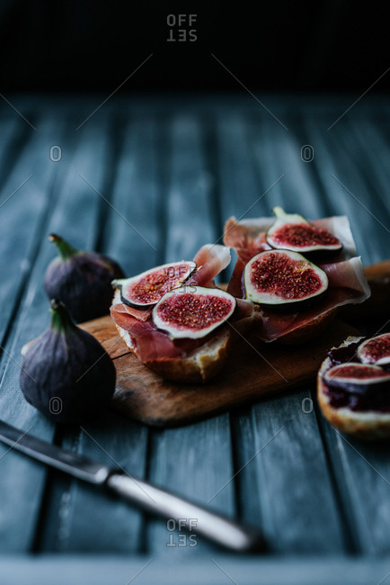 Bread with ham and fresh figs served on a wooden plate on blue background