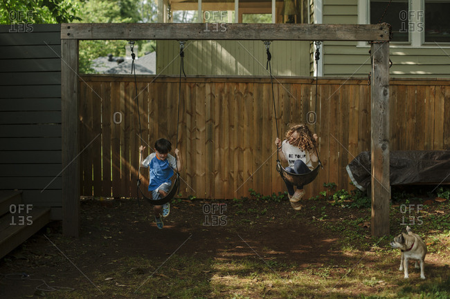 Two children swinging in sync in a backyard