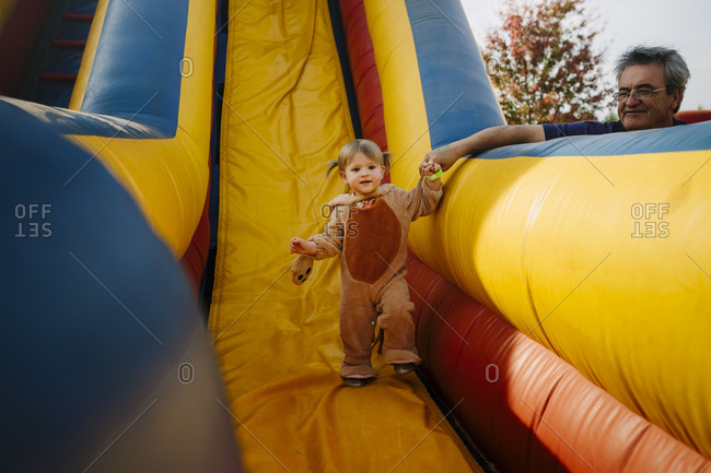 Grandfather helping granddaughter walk down inflatable slide