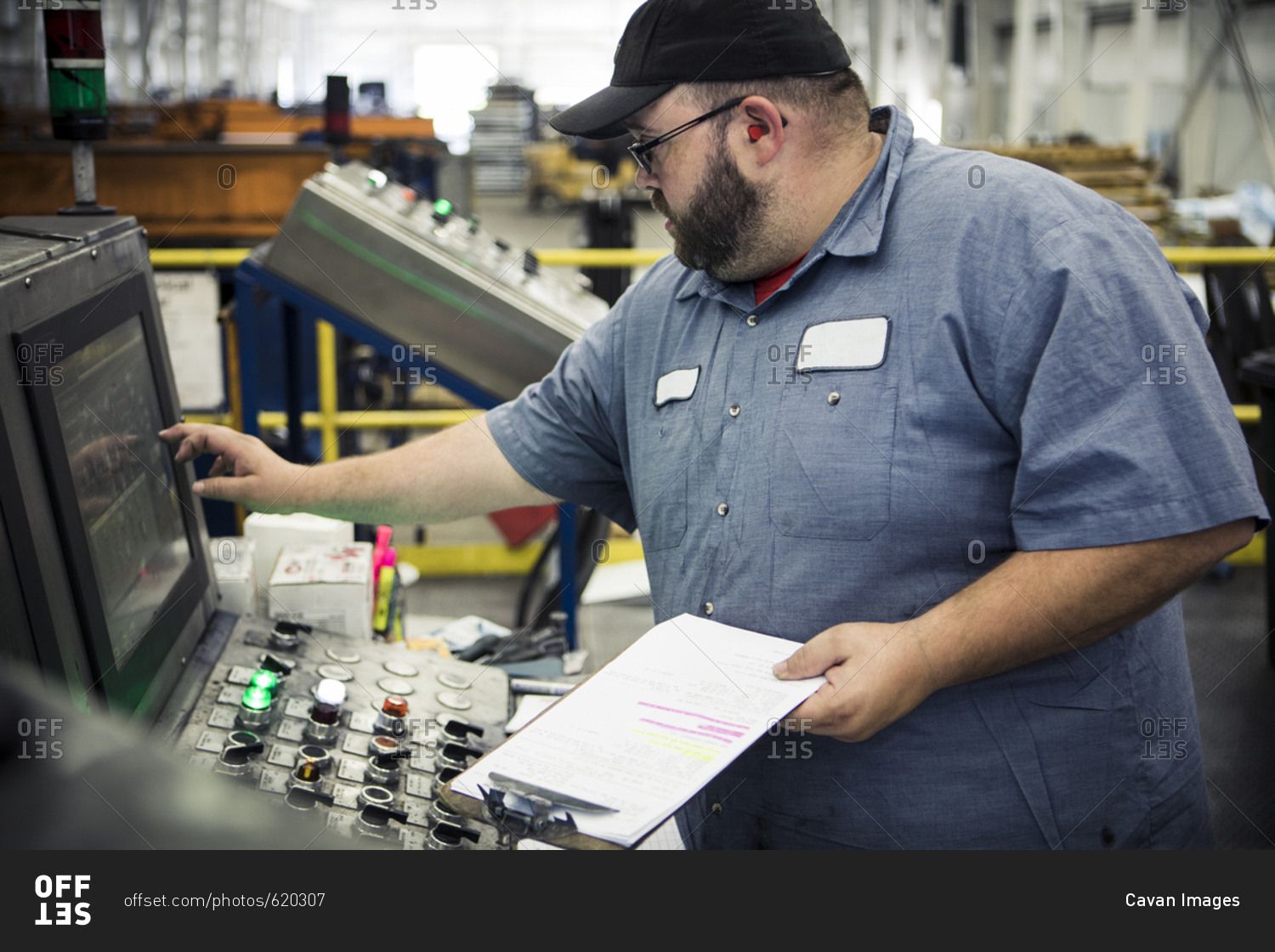 Overweight manual worker operating machinery at control panel in metal industry
