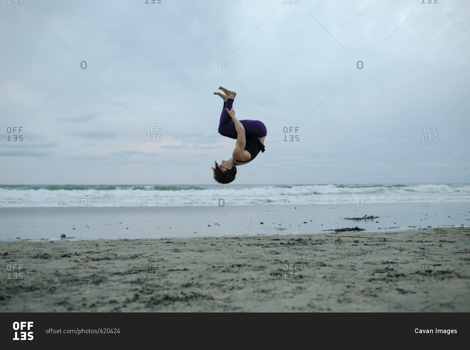 Carefree woman back flipping at beach while exercising against sky