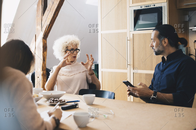 Senior businesswoman explaining to male colleague while sitting at table with breakfast in office