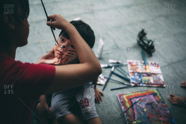 Woman applying cat-like face paint to a toddler's face