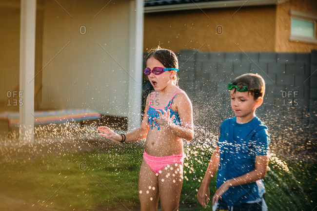 Siblings stand in sprinkler