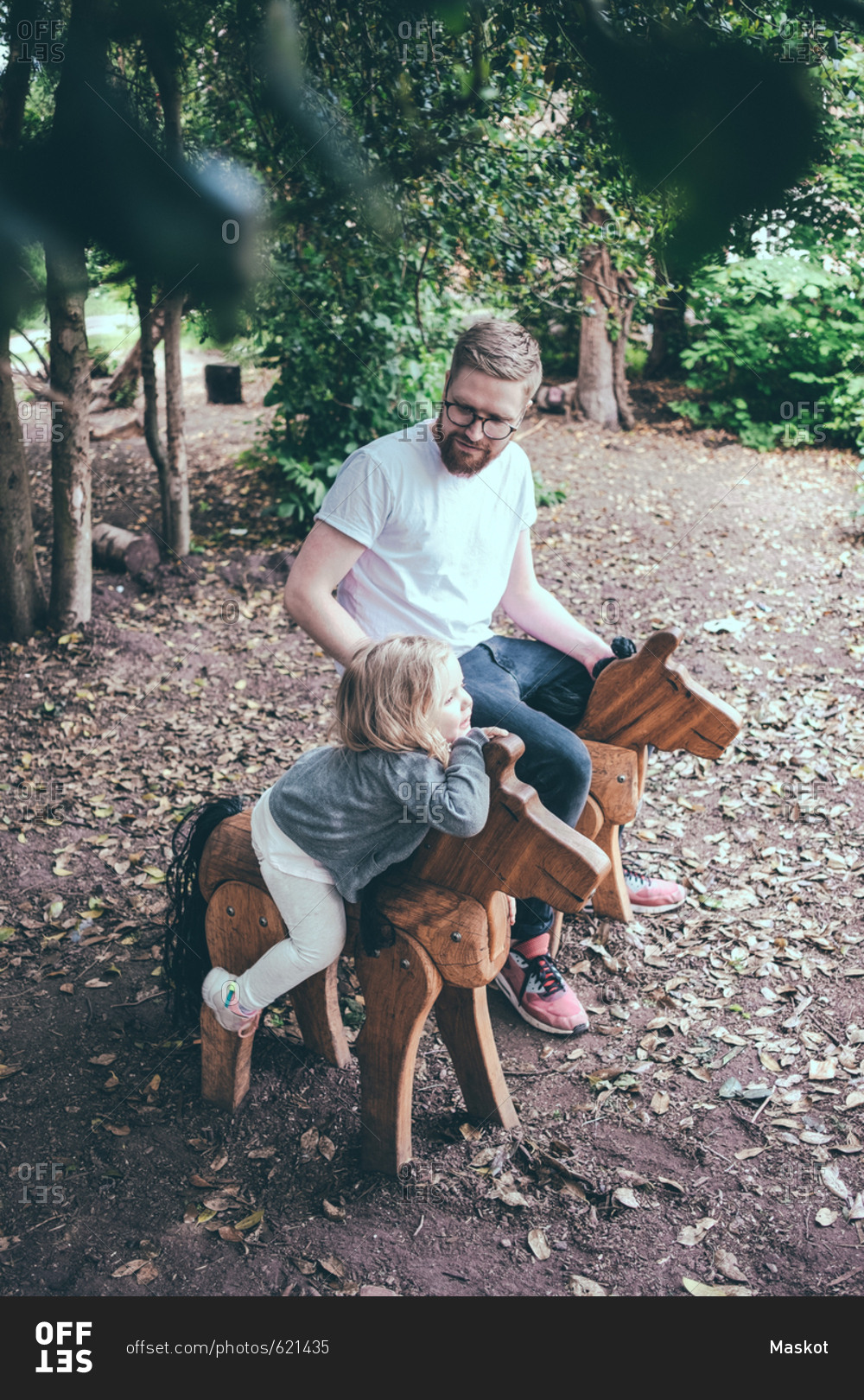 High angle view of father and daughter sitting on wooden horses at park