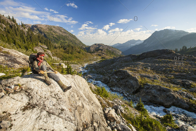 A mountaineer sits on a boulder above a rushing river, Garibaldi Provincial Park