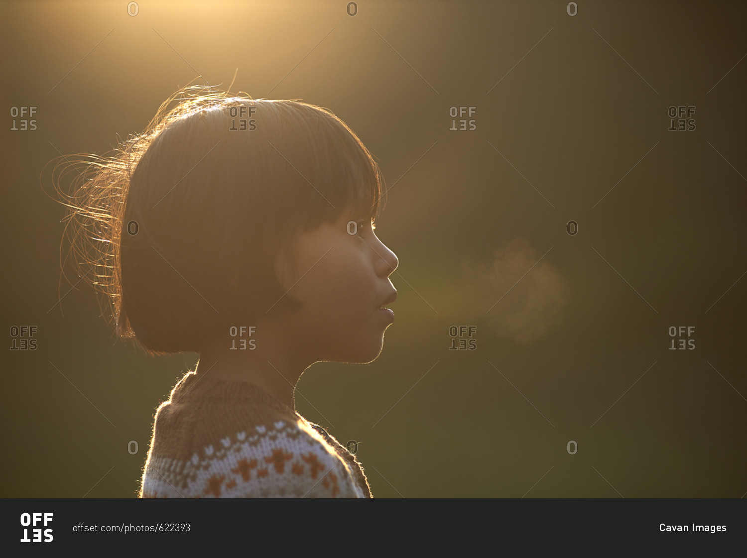 Close-up of girl exhaling breath vapor while looking away during sunny day in winter