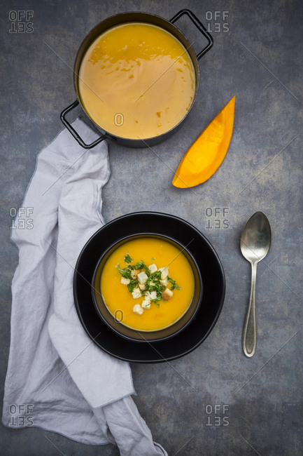 Soup dish of creamed pumpkin soup with croutons and parsley and pumpkin soup in cooking pot