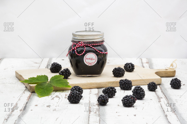 Glass of homemade blackberry jam- blackberries and leaf on wooden board