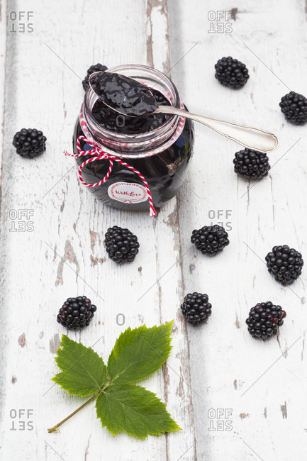 Glass of homemade blackberry jam- blackberries and leaf on wood